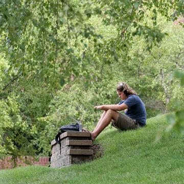 A student sits on the hill on campus and listens to music through headphones.